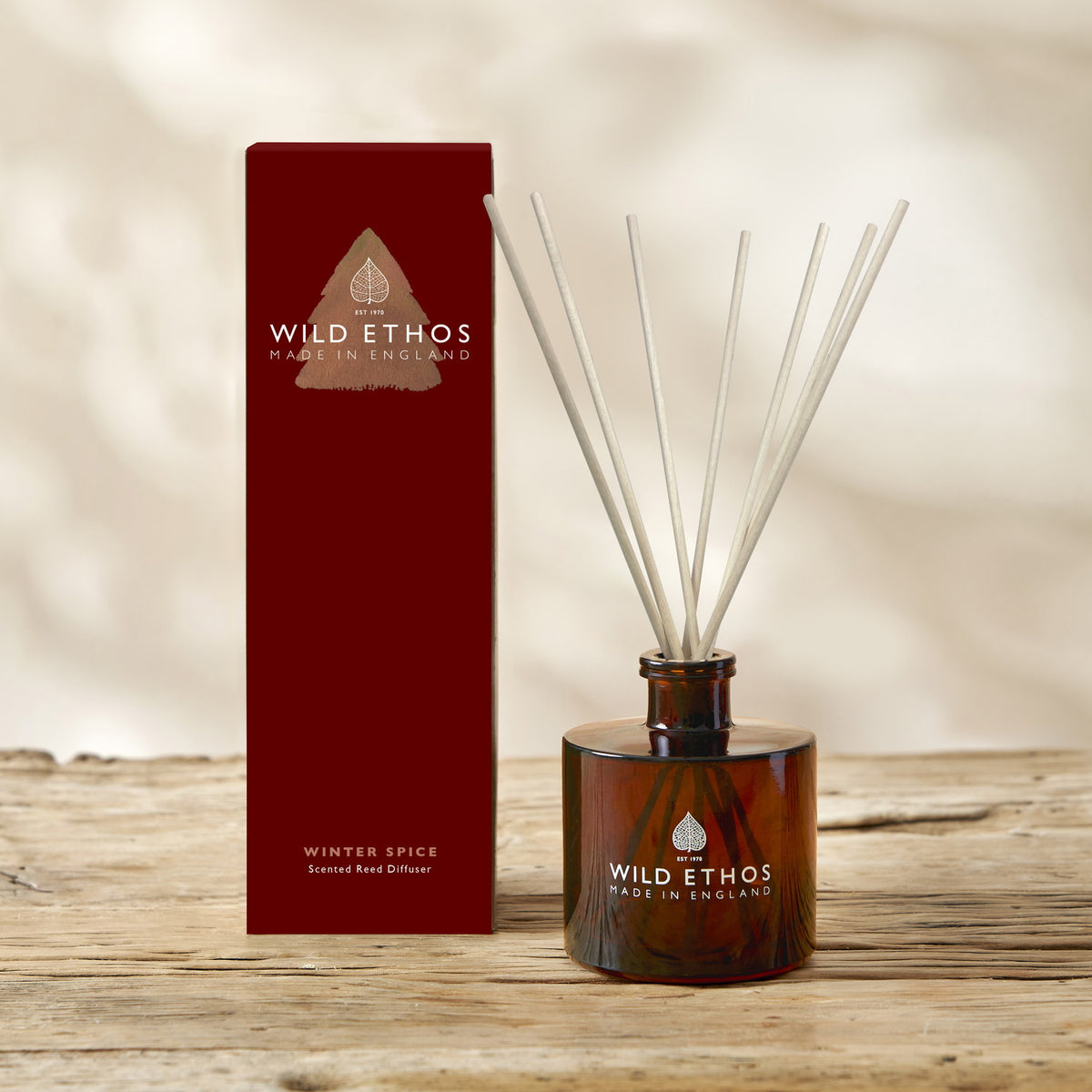 Wild Ethos Winter Spice scented reed diffuser in an amber glass bottle with reeds, beside its tall red gift box